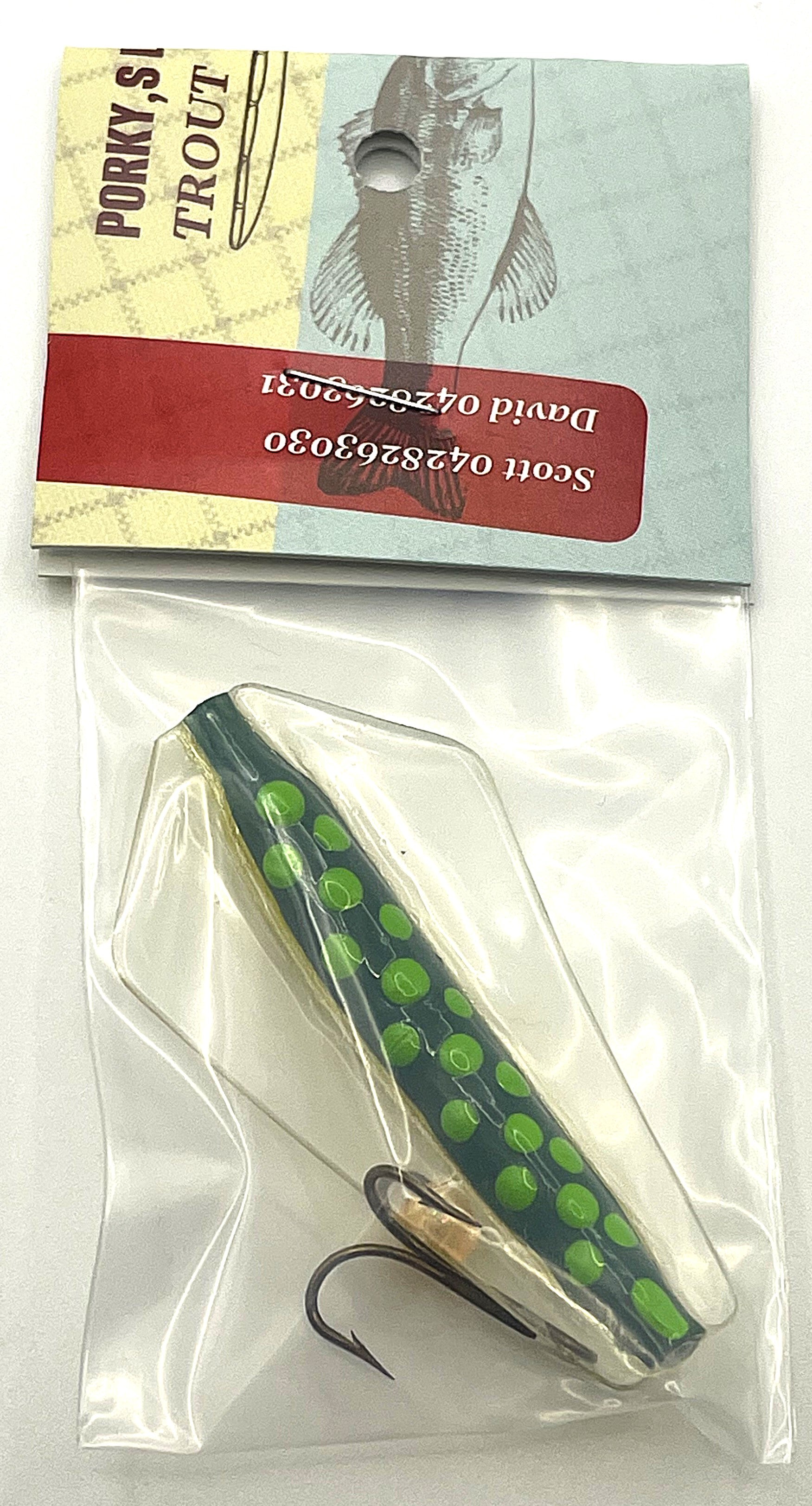 Fishing lure thjat is dark green with light green spots and packaging 